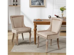 Conjunto de 2 sillas de terciopelo beige con patas de madera curvadas y remaches dorados.