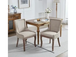 Juego de 2 sillas beige con patas de madera curvadas y ribete de tachuelas.
